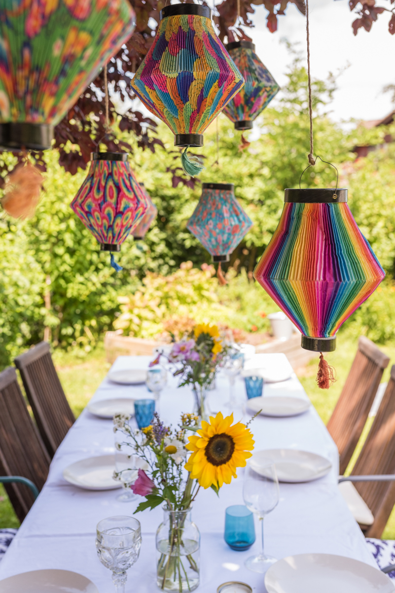 Dekoideen für die Gartenparty im Sommer mit bunten Lampions und Blumen und Leckereien vom Grillbüfett